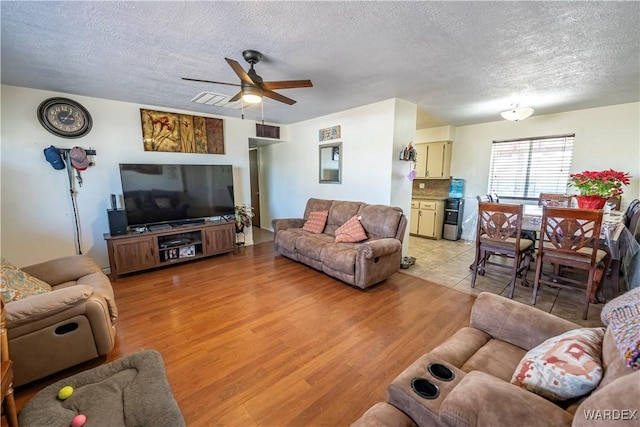 living room featuring light wood-style floors, visible vents, a textured ceiling, and a ceiling fan