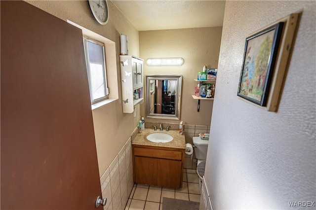 bathroom featuring wainscoting, toilet, tile patterned flooring, vanity, and tile walls