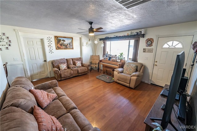 living area with a ceiling fan, a textured ceiling, visible vents, and wood finished floors