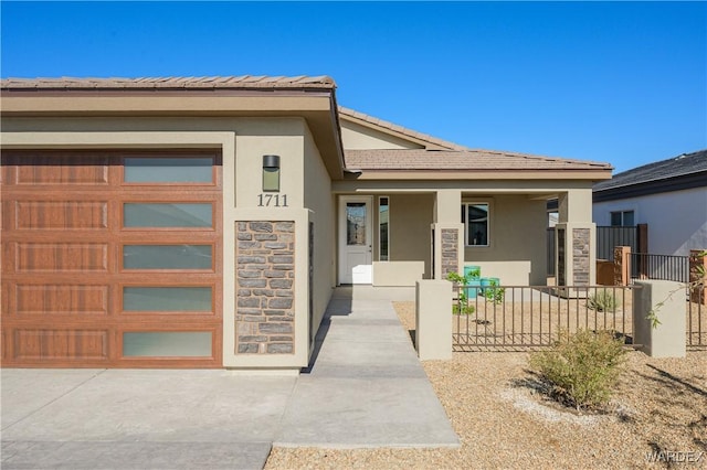 view of exterior entry featuring an attached garage, fence, stone siding, a tiled roof, and stucco siding