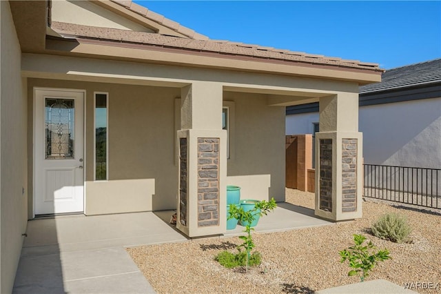 entrance to property with a patio area, fence, and stucco siding