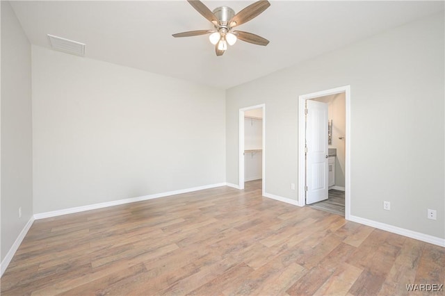 unfurnished bedroom featuring baseboards, visible vents, a walk in closet, light wood-type flooring, and a closet