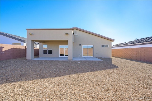 rear view of property with stucco siding, a fenced backyard, and a patio