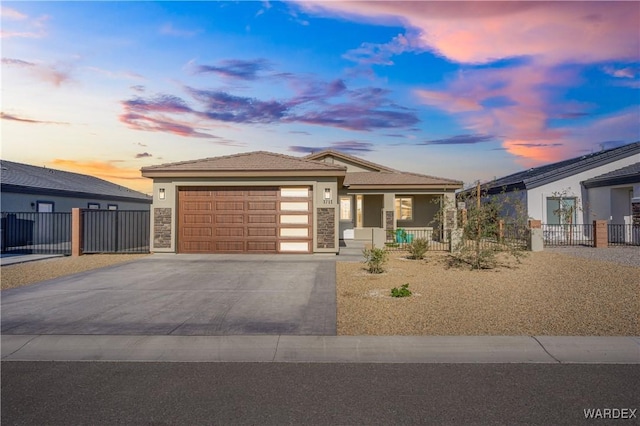 prairie-style house with stone siding, concrete driveway, fence, and an attached garage