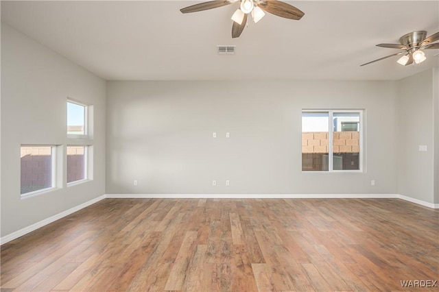 empty room featuring a healthy amount of sunlight, baseboards, visible vents, and wood finished floors