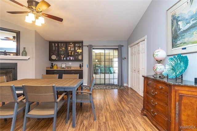 dining room with a ceiling fan, vaulted ceiling, a fireplace, and wood finished floors