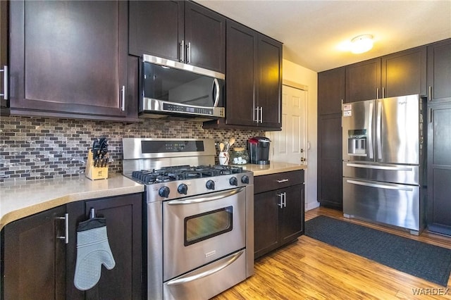 kitchen featuring light wood finished floors, tasteful backsplash, stainless steel appliances, and light countertops