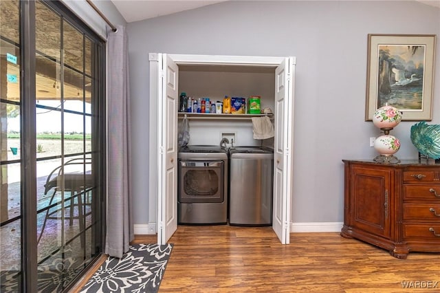 clothes washing area featuring laundry area, wood finished floors, washing machine and dryer, and baseboards