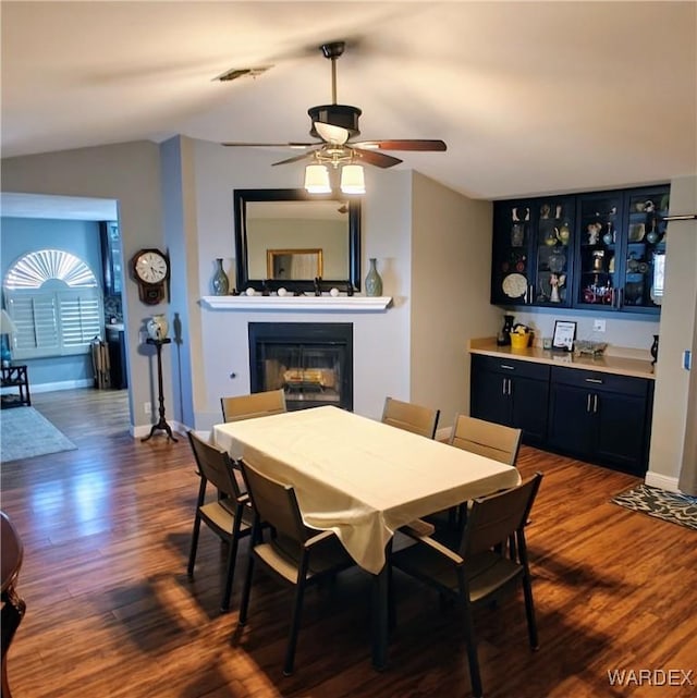 dining space with lofted ceiling, baseboards, dark wood-type flooring, and a glass covered fireplace