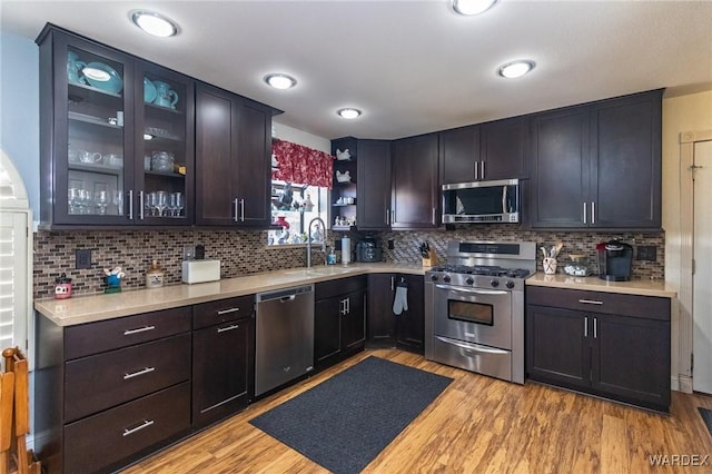 kitchen with a sink, light wood-style floors, light countertops, appliances with stainless steel finishes, and tasteful backsplash