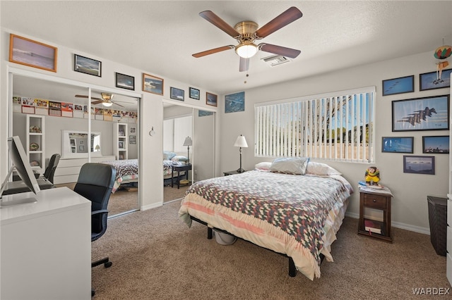 bedroom with visible vents, ceiling fan, a textured ceiling, carpet flooring, and two closets