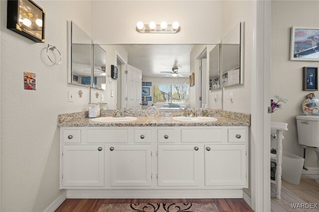 bathroom featuring toilet, ceiling fan, double vanity, and a sink