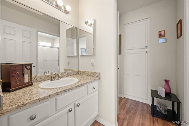 full bath featuring a shower with shower door, baseboards, wood finished floors, and vanity