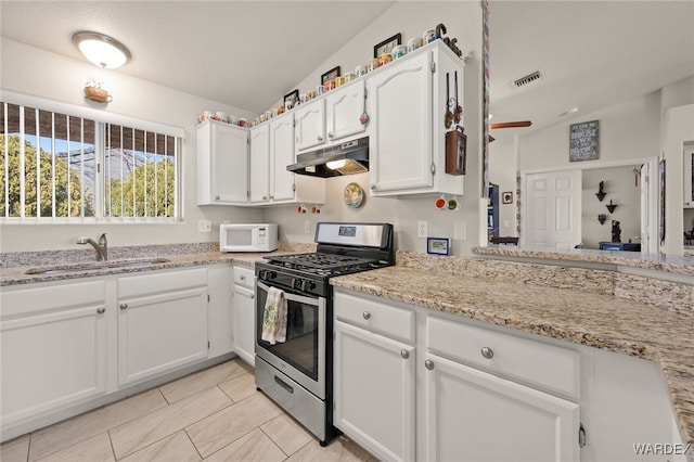 kitchen featuring stainless steel gas range oven, white microwave, under cabinet range hood, a sink, and white cabinets