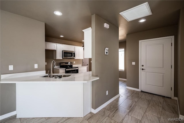 kitchen with a peninsula, appliances with stainless steel finishes, a sink, and light countertops