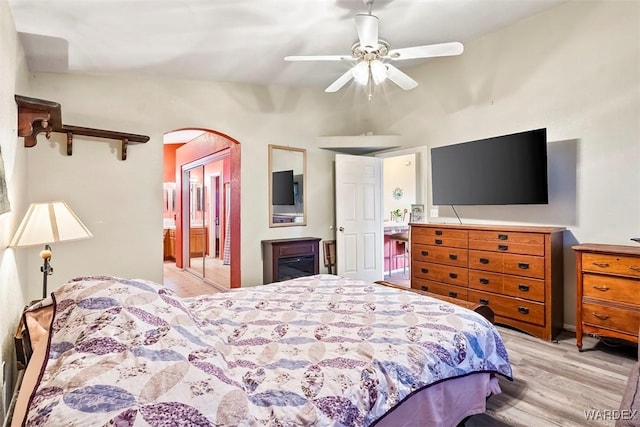 bedroom with arched walkways, ceiling fan, ensuite bathroom, and light wood finished floors