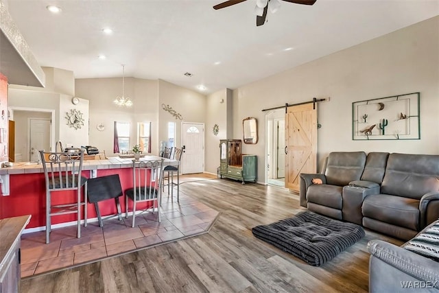 living area featuring a barn door, wood finished floors, vaulted ceiling, and ceiling fan with notable chandelier