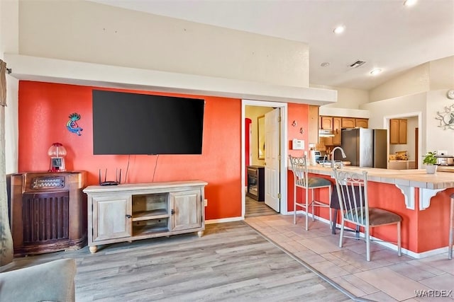 kitchen with tile counters, a kitchen breakfast bar, freestanding refrigerator, and vaulted ceiling