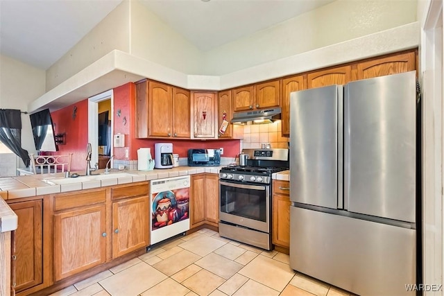 kitchen with light tile patterned floors, a sink, stainless steel appliances, under cabinet range hood, and brown cabinets