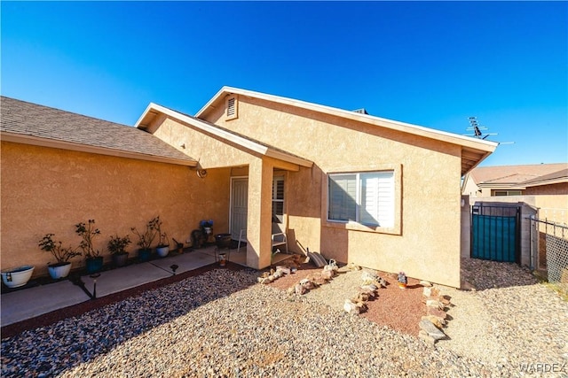 exterior space with stucco siding, a patio, roof with shingles, and fence