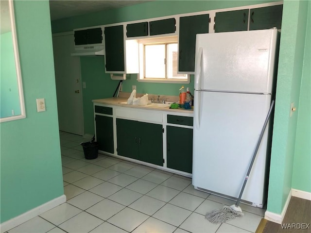 kitchen featuring dark cabinets, freestanding refrigerator, light countertops, and baseboards