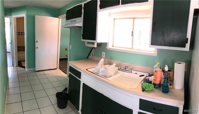 kitchen featuring light tile patterned floors, dark cabinets, light countertops, under cabinet range hood, and a sink