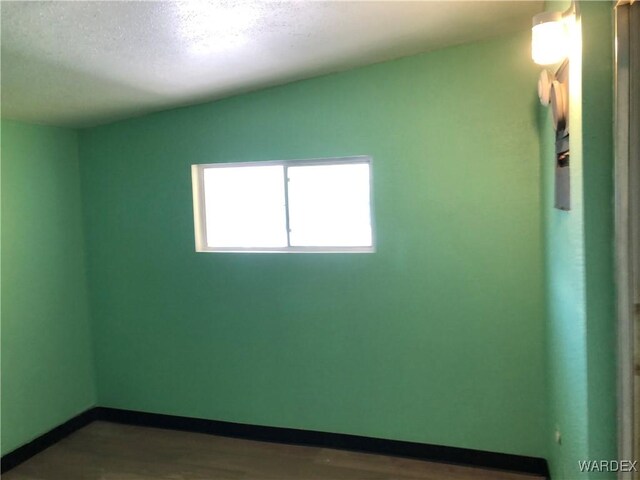 empty room with a textured ceiling, baseboards, and wood finished floors