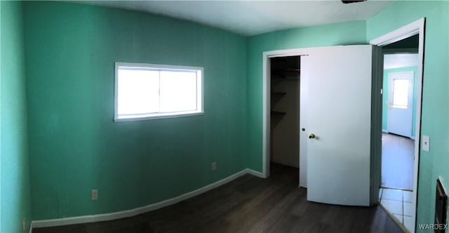 unfurnished bedroom featuring a closet, dark wood-style flooring, multiple windows, and baseboards