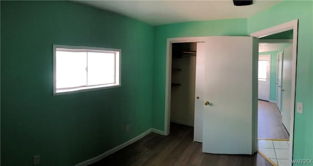 unfurnished bedroom with dark wood-type flooring, multiple windows, a closet, and baseboards