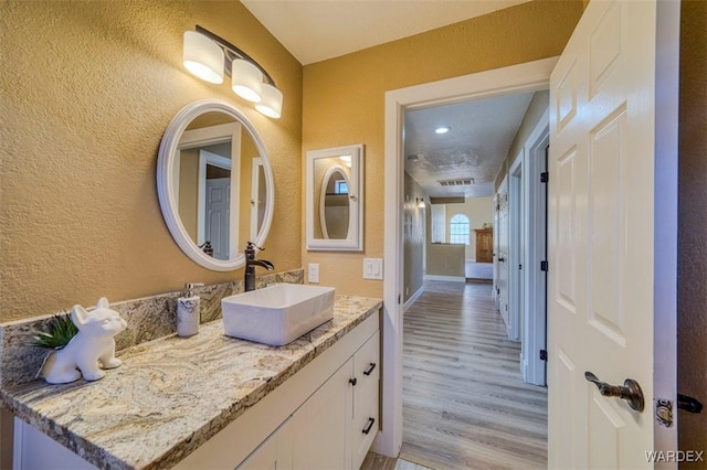 bathroom with a textured wall, wood finished floors, visible vents, vanity, and baseboards