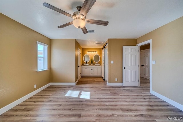 unfurnished bedroom featuring ensuite bath, light wood finished floors, baseboards, and visible vents