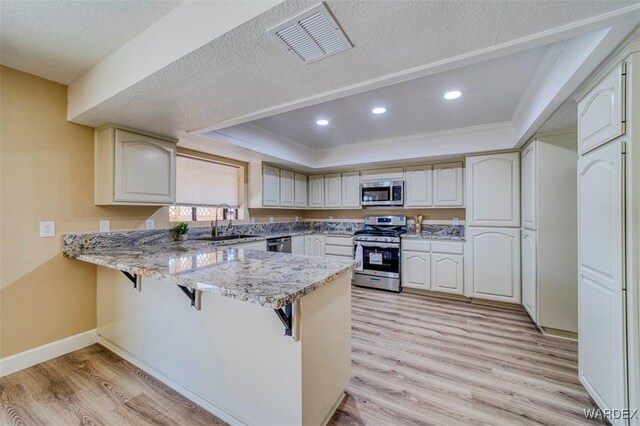 kitchen with a breakfast bar area, a peninsula, a sink, visible vents, and appliances with stainless steel finishes