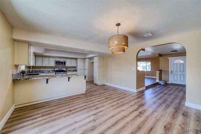 kitchen with light stone counters, arched walkways, hanging light fixtures, appliances with stainless steel finishes, and a peninsula