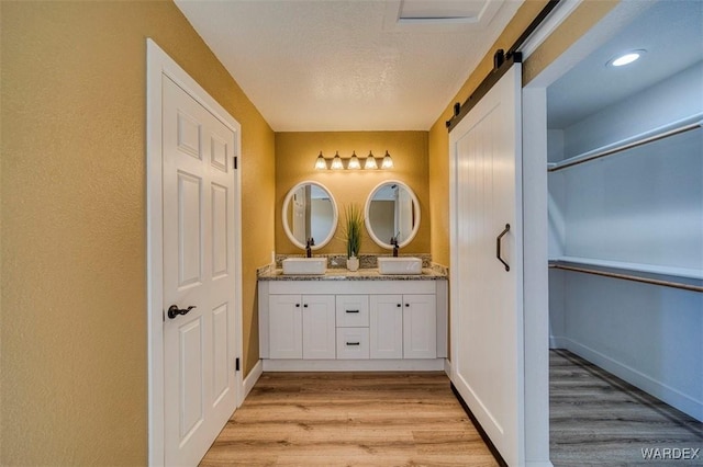 bathroom featuring a sink, a textured ceiling, double vanity, and wood finished floors