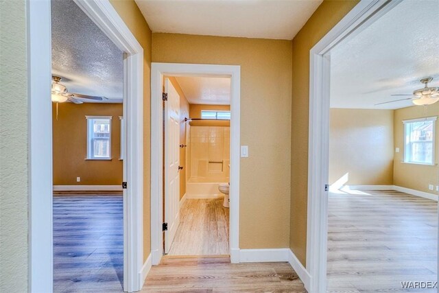 hallway with light wood-style flooring, baseboards, and a textured ceiling