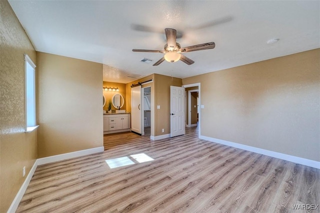 unfurnished bedroom with light wood-style floors, visible vents, baseboards, and a barn door