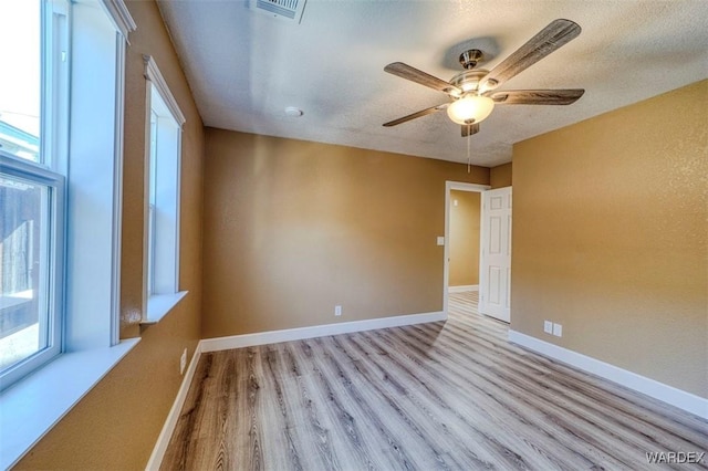 empty room featuring light wood finished floors, visible vents, a ceiling fan, a textured ceiling, and baseboards