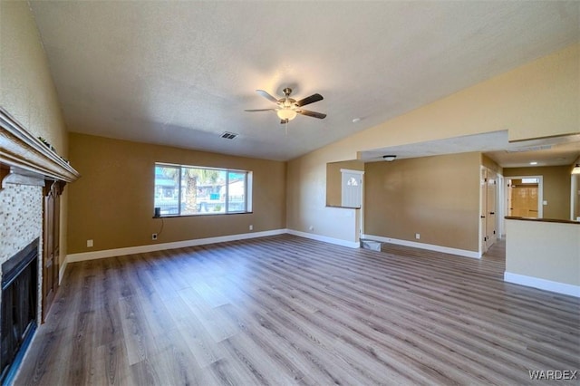 unfurnished living room with ceiling fan, a tile fireplace, vaulted ceiling, and wood finished floors