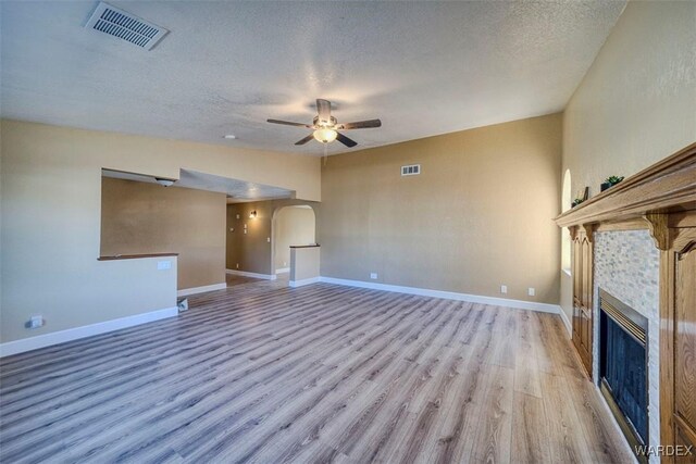 unfurnished living room with arched walkways, light wood-style flooring, a tiled fireplace, and visible vents