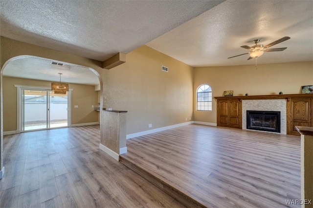 unfurnished living room featuring light wood-type flooring, arched walkways, a fireplace, and a textured ceiling