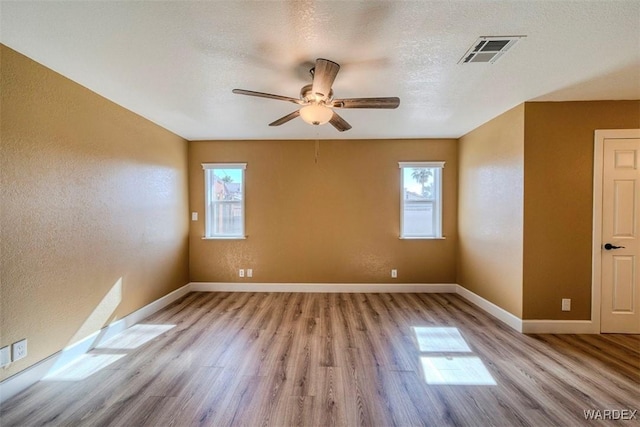 spare room with a textured ceiling, a textured wall, visible vents, baseboards, and light wood-style floors