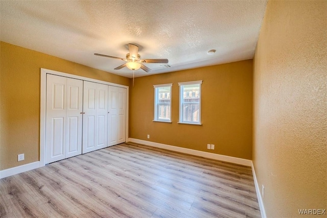 unfurnished bedroom featuring a textured ceiling, light wood-style floors, a closet, and baseboards