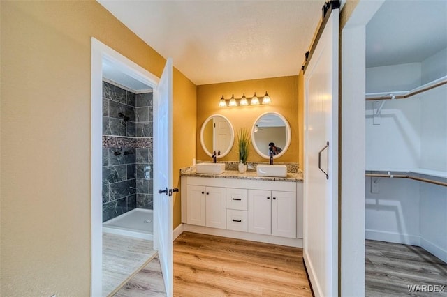 bathroom featuring a walk in closet, double vanity, a sink, a shower stall, and wood finished floors