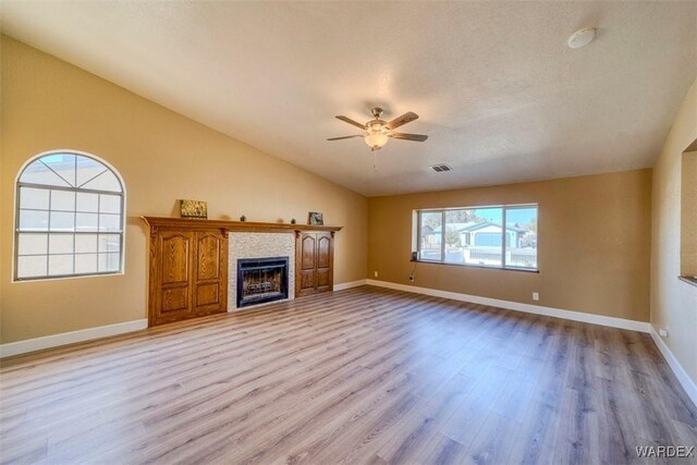 unfurnished living room with light wood finished floors, baseboards, lofted ceiling, ceiling fan, and a fireplace