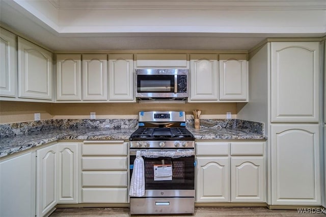 kitchen with appliances with stainless steel finishes, dark stone counters, and light wood-type flooring