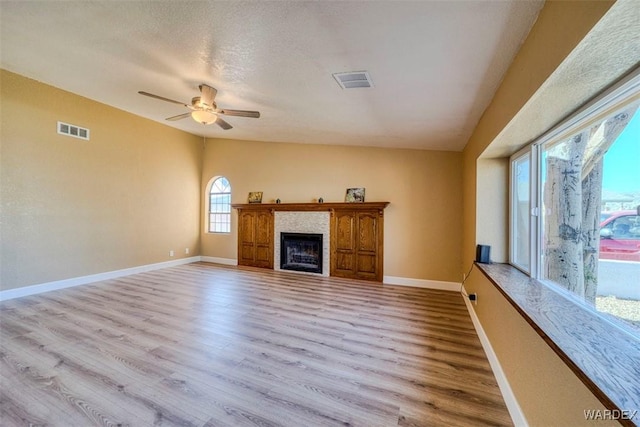 unfurnished living room with baseboards, visible vents, a tile fireplace, lofted ceiling, and light wood-style floors