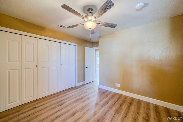 unfurnished bedroom featuring ceiling fan, light wood-style flooring, visible vents, baseboards, and a closet