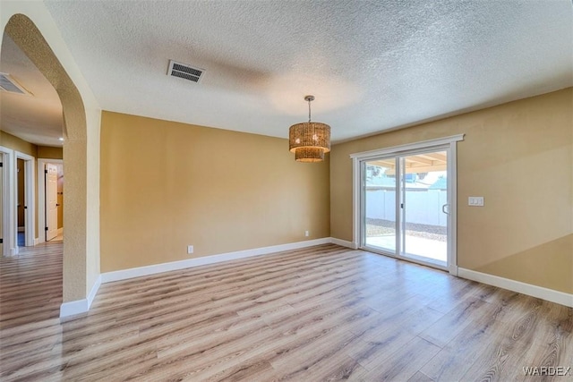 empty room featuring arched walkways, light wood-type flooring, visible vents, and baseboards