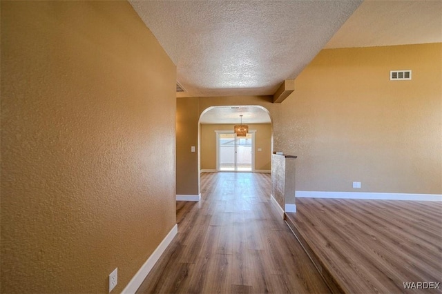 hallway with arched walkways, visible vents, baseboards, and wood finished floors