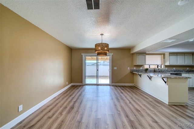 kitchen with light wood finished floors, a peninsula, a breakfast bar, and decorative light fixtures